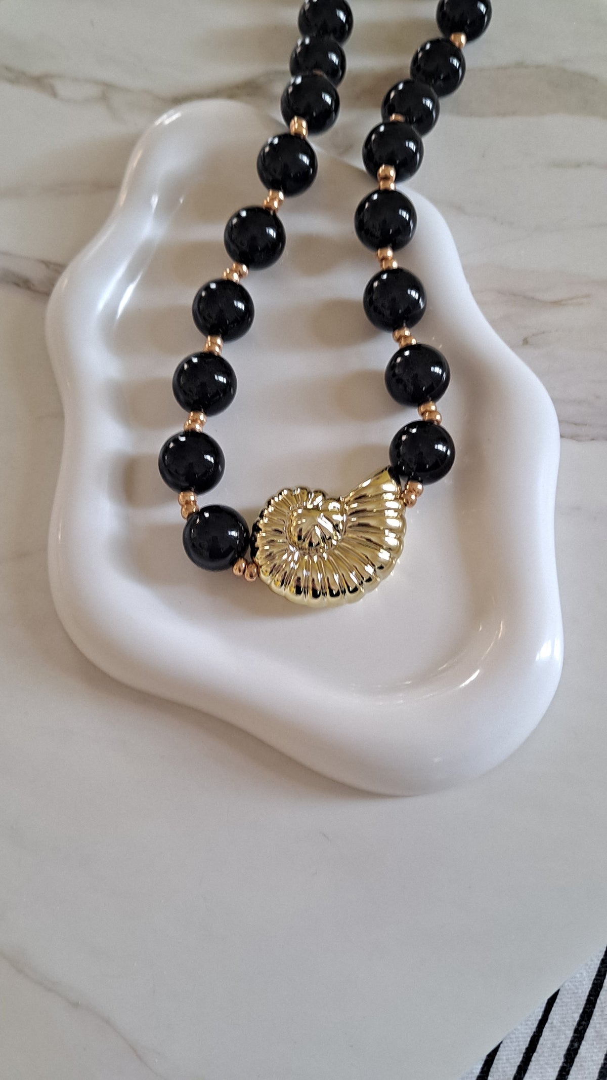 Collar negro en acrilico acompañado por un shell dorado perfecto para ir de viaje o a la playa